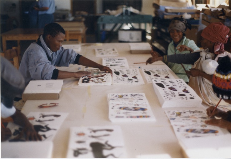 Kuru Art Project artists sitting at a table signing their lithographs which are included in Qauqaua.