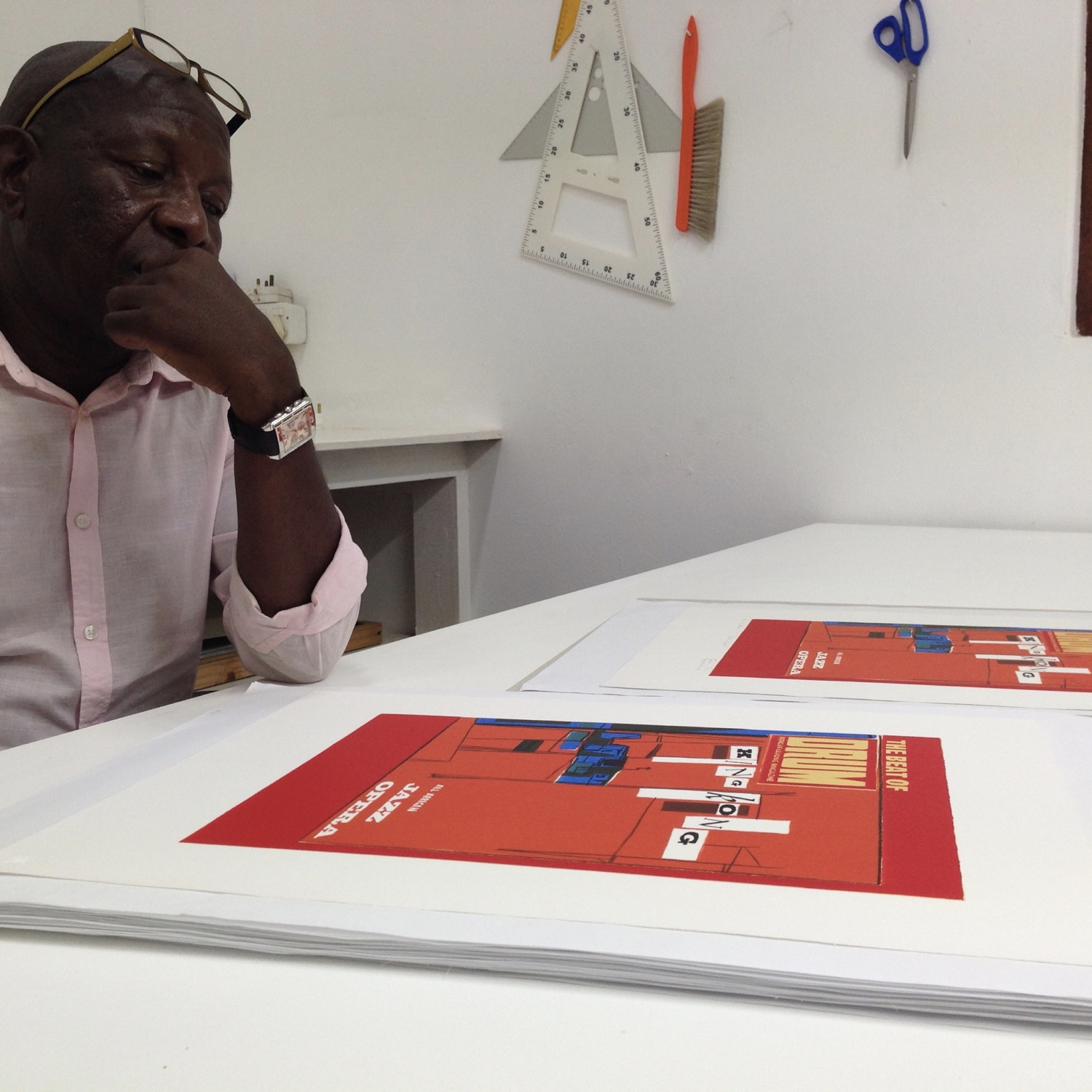 Artist Sam Nhlengethwa sitting at table looking at his limited edition prints  based on Drum Magazine