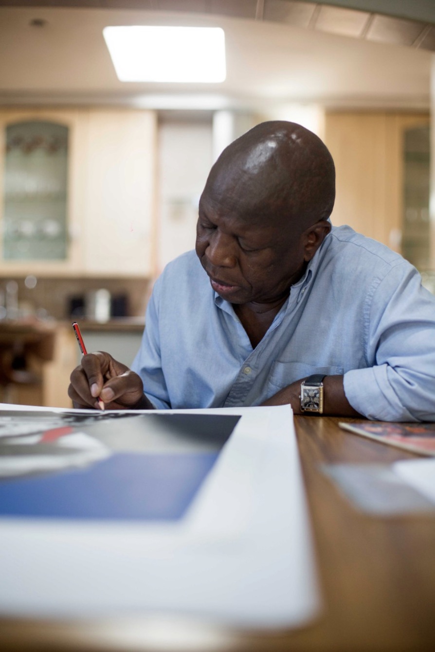Artist Sam Nhlengethwa signing his jazz lithographs printed by The Artists' Press at a table.